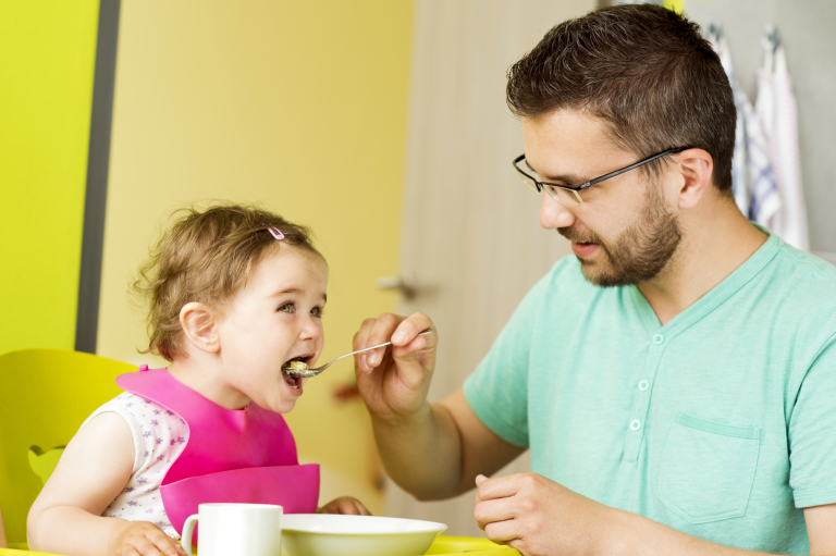 Father feeding daughter on high chair